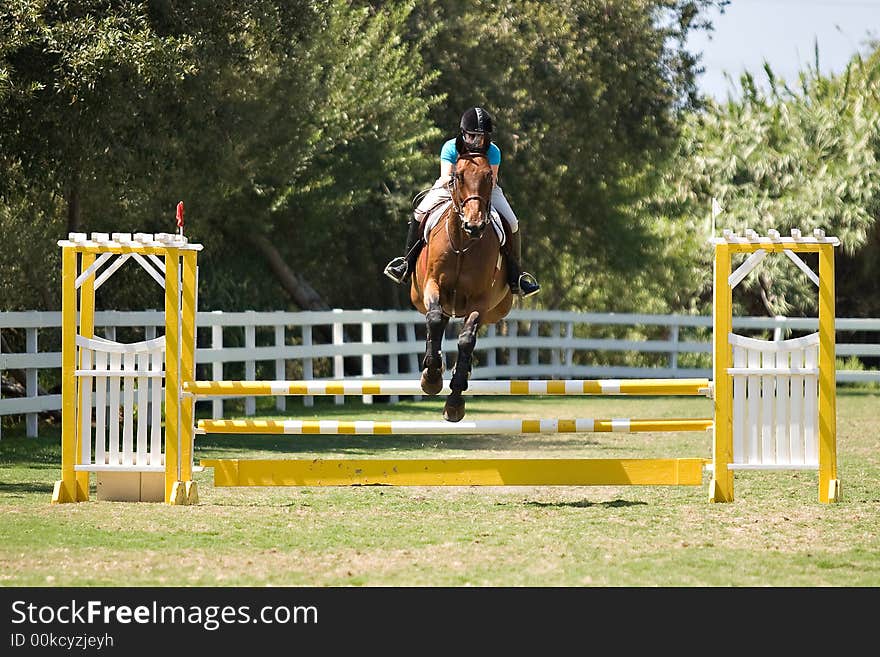 A youth rider guiding her horse over a fence in a show jumping competition. A youth rider guiding her horse over a fence in a show jumping competition.