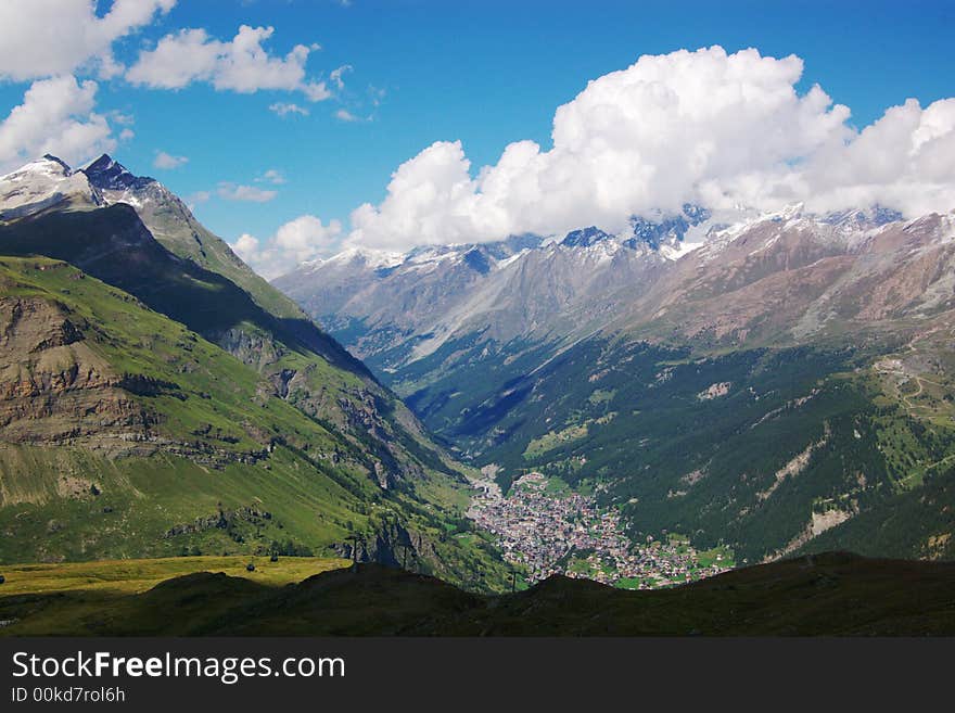 A panoramic view on Swiss Alps rocky mountains with village in valley under cloudy sky, horizontal. Zermat, Switzerland, Europe. A panoramic view on Swiss Alps rocky mountains with village in valley under cloudy sky, horizontal. Zermat, Switzerland, Europe.