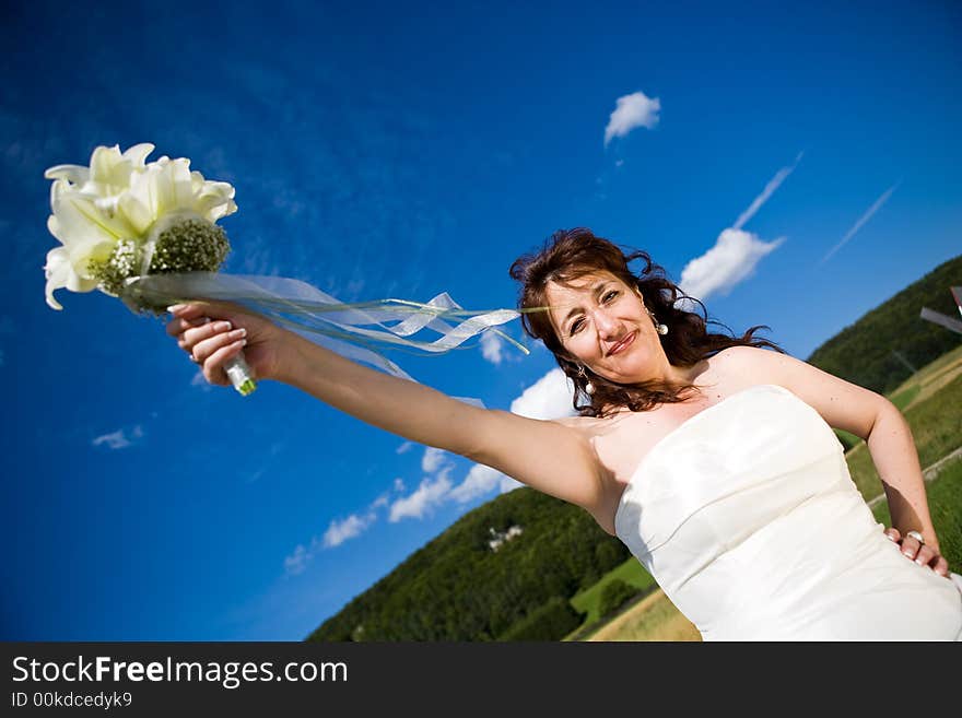 Fancy Perspective. Bride holds her bridal bouquet on outstretched arm. Deep blue sky as background. Sunny weather. Adult bride. Fancy Perspective. Bride holds her bridal bouquet on outstretched arm. Deep blue sky as background. Sunny weather. Adult bride.