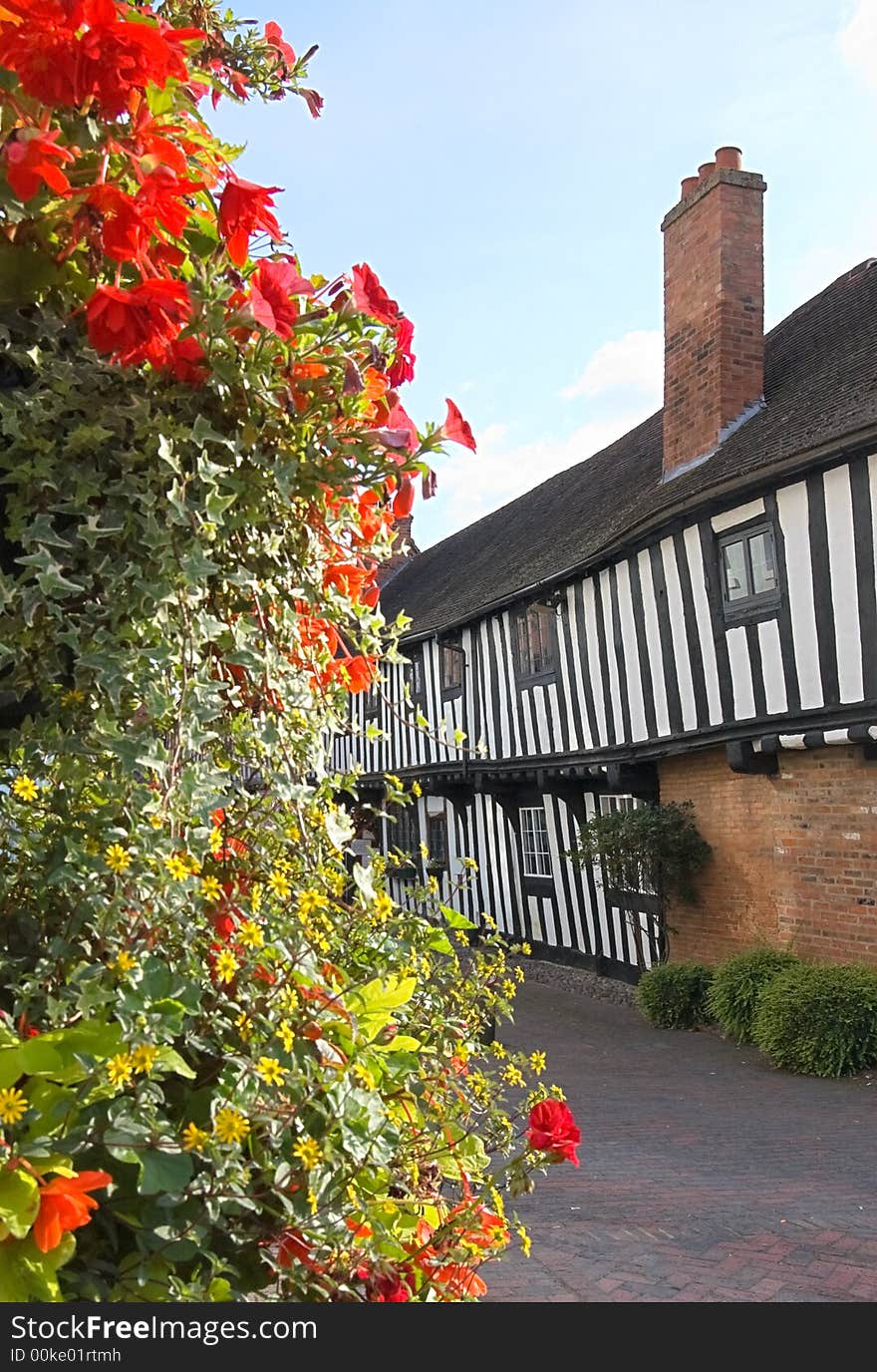 Half timbered Tudor cottages framed by a large display of flowers and shrubs. Focus on the cottages.