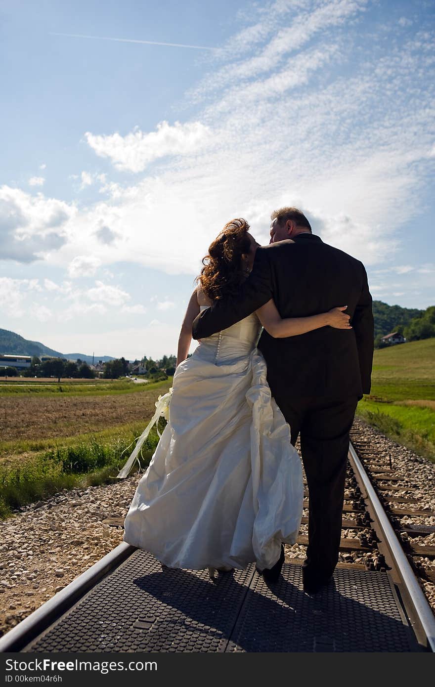 Bridal Couple (over 40 years old) amorous from the back. They are hugging each other while standing on a railway track. It is summer, great sky. Bridal Couple (over 40 years old) amorous from the back. They are hugging each other while standing on a railway track. It is summer, great sky.