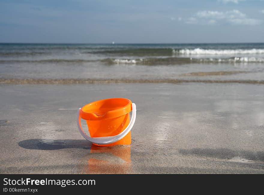 Brigh orange sand bucket with water on the beach. Brigh orange sand bucket with water on the beach