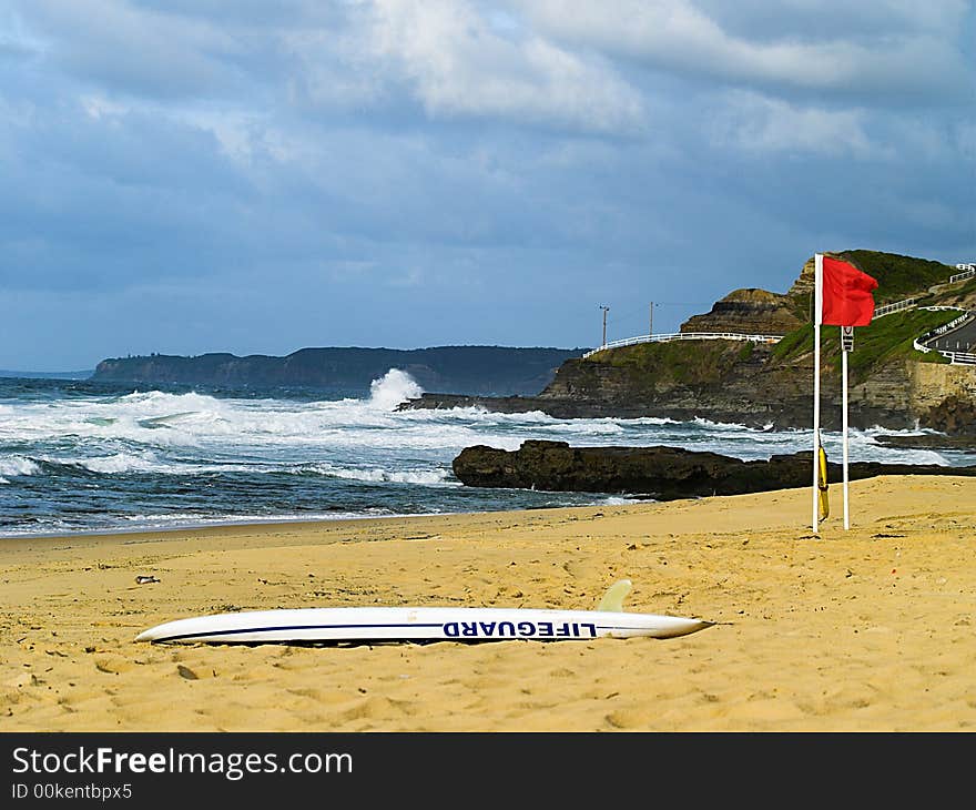 An empty beach with the lifeguard rescue board on the sand and red closed flag. An empty beach with the lifeguard rescue board on the sand and red closed flag