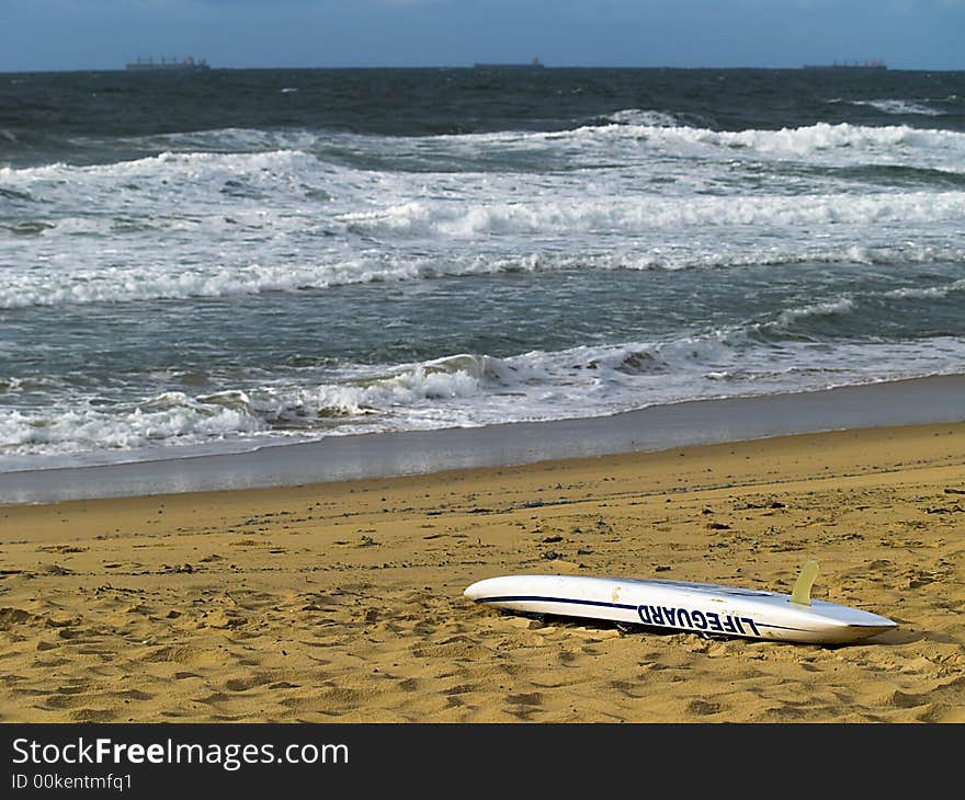 A lifeguard rescue board on the beach with ships on the distant horizon