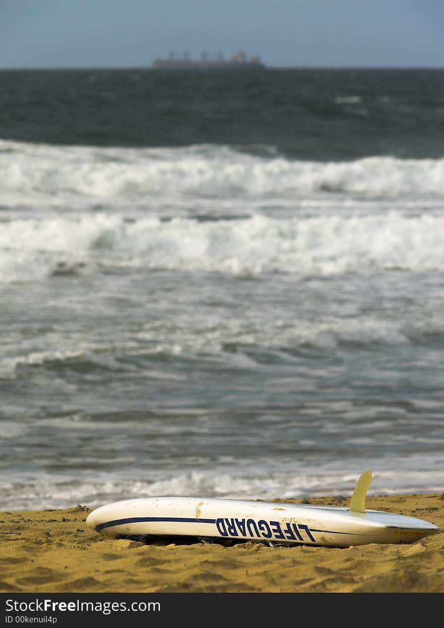 A lifeguard rescue board on the beach with a ship on the horizon