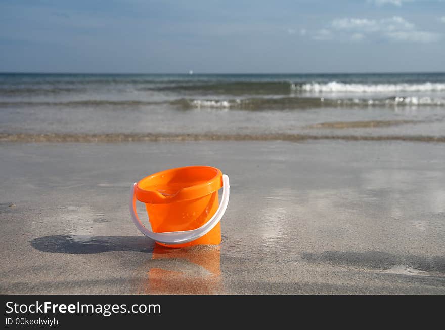 Brigh orange sand bucket with water on the beach. Brigh orange sand bucket with water on the beach