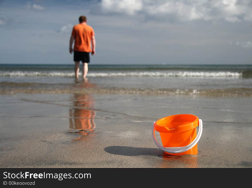 Brigh orange sand bucket with water on the beach and boy on the background. Brigh orange sand bucket with water on the beach and boy on the background