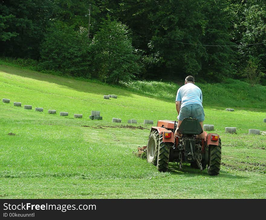 Men with tractor work in the green grass park field