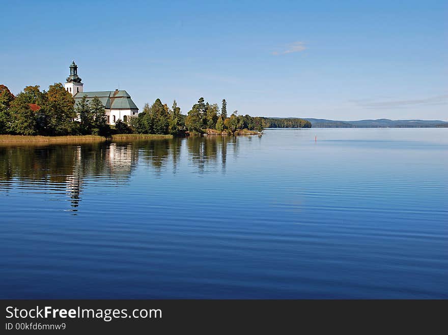 A lake in sweden,reflection of the church and trees in the calm water.Scenic view of a little hills in the background. A lake in sweden,reflection of the church and trees in the calm water.Scenic view of a little hills in the background.