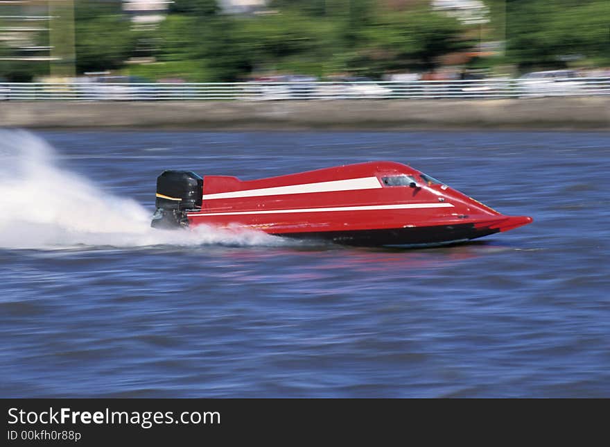 A red outboard of competition at full speed on blue water of a river.