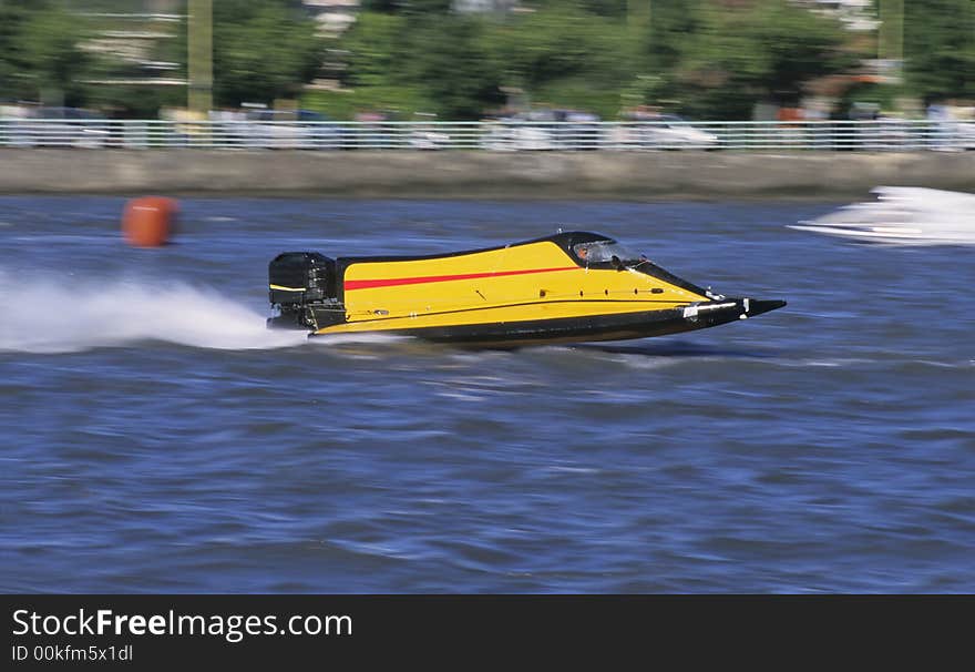 A yellow outboard of competition at full speed on blue water of a river.