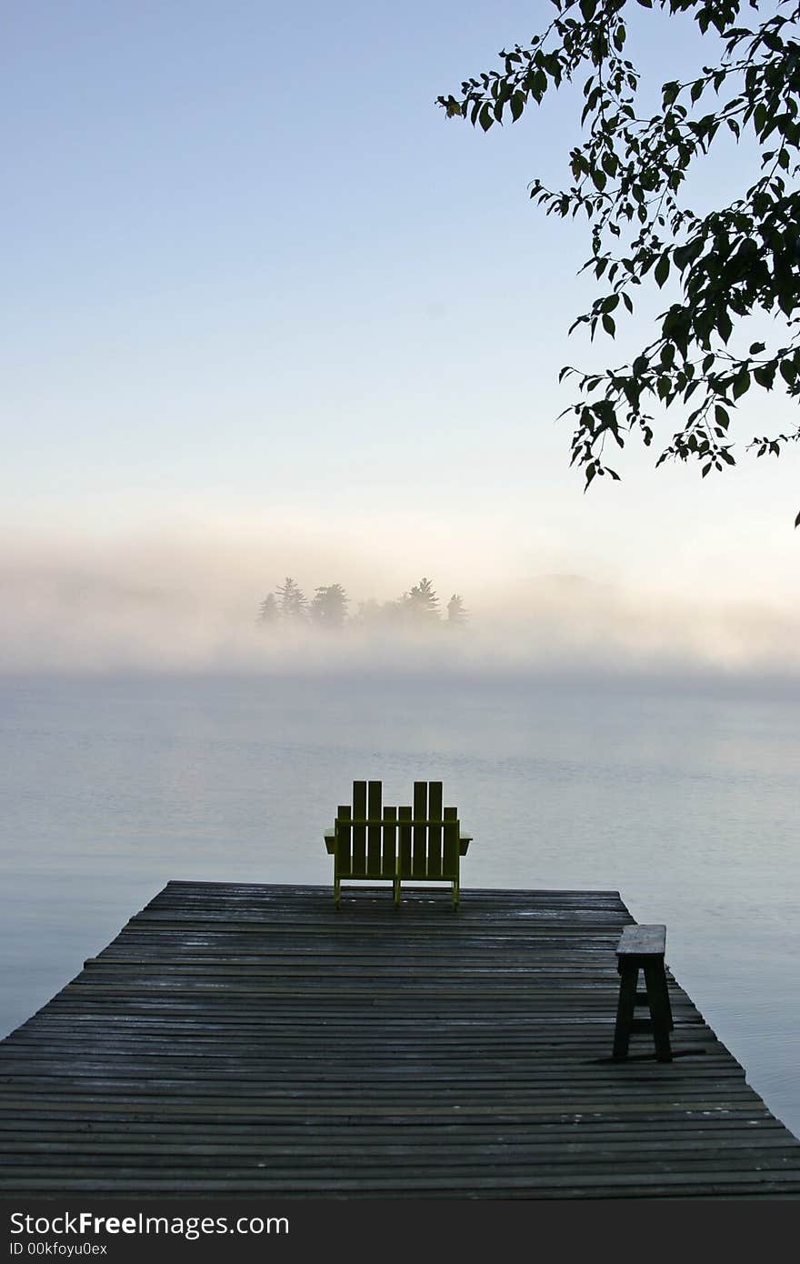 A chair by a misty lake early in the morning. A chair by a misty lake early in the morning.