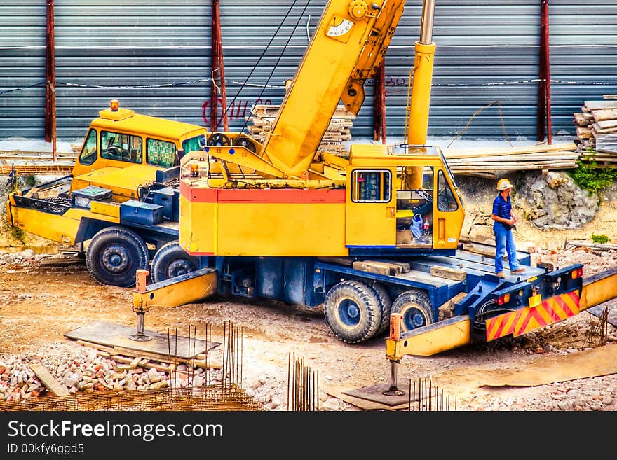 A crane operator rests outside his machine at a work site while waiting for the other works to be ready. A crane operator rests outside his machine at a work site while waiting for the other works to be ready.