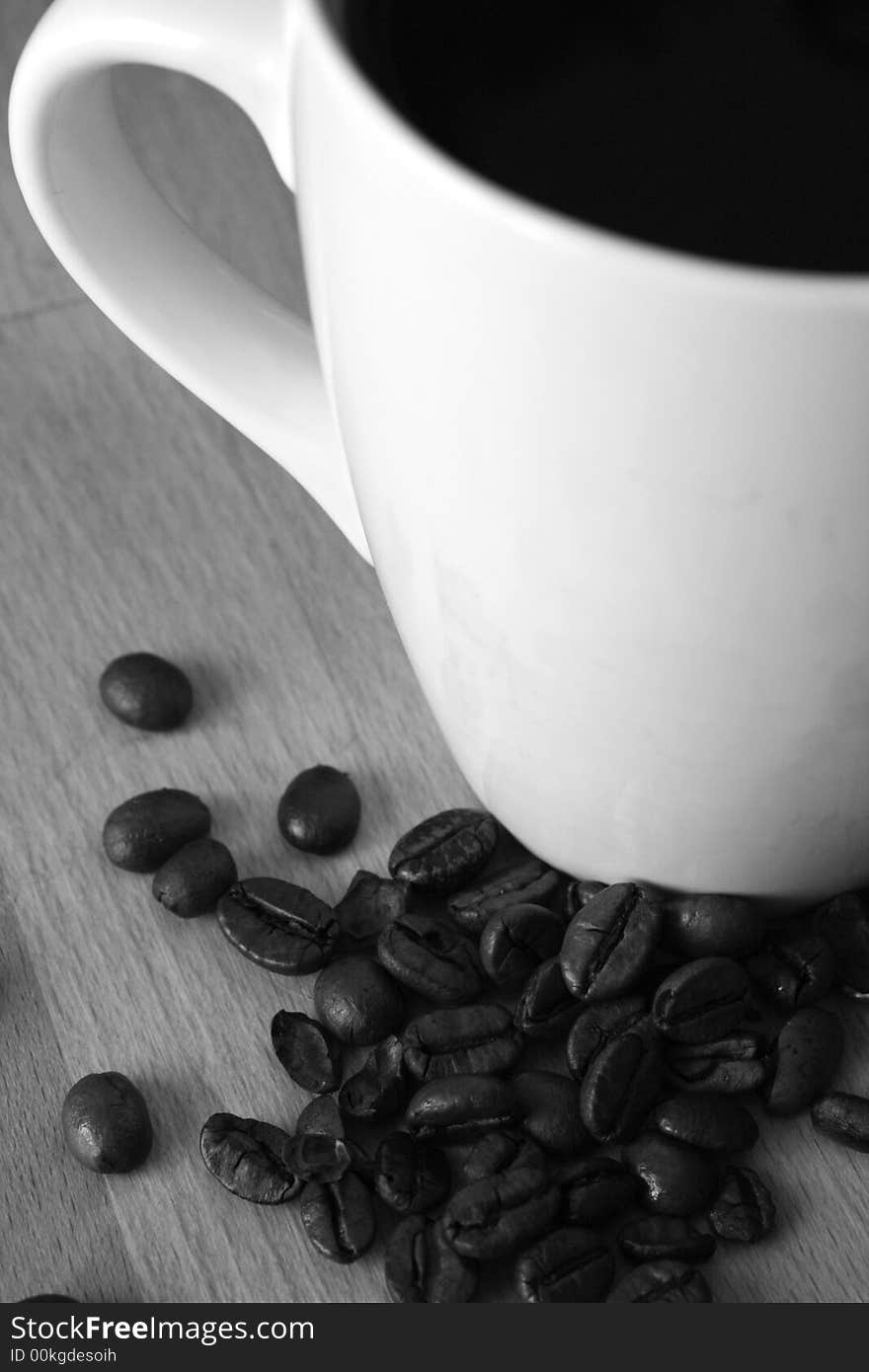Black coffee in a white mug with roasted coffee beans spread around,black and white image