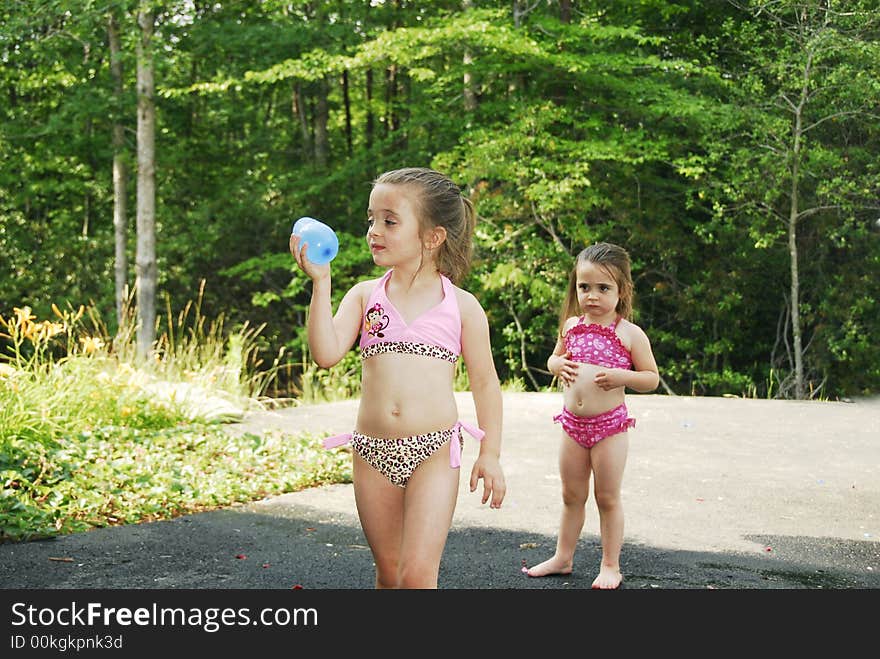 Cute little girls dressed in their swimsuits getting ready to throw a water balloon. Cute little girls dressed in their swimsuits getting ready to throw a water balloon.