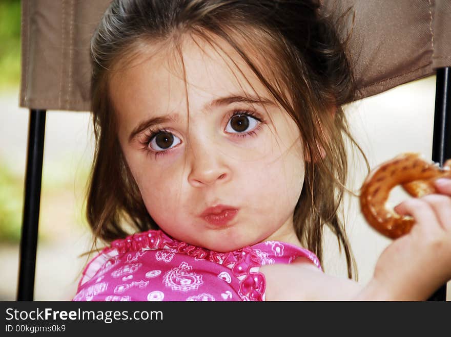 Cute little girl eating a big pretzel in an outdoor setting. Cute little girl eating a big pretzel in an outdoor setting.