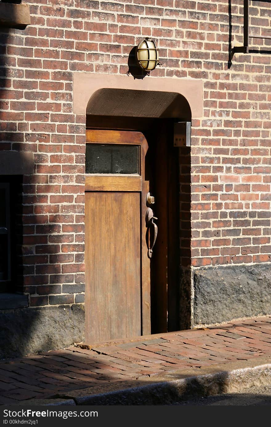 Old wooden basement door inset in brick wall, strong shadow in beacon hill area of boston