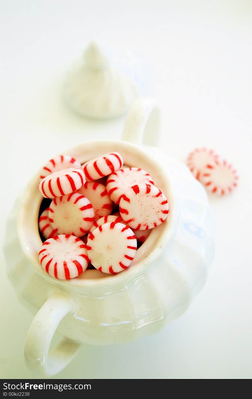 Red and white hard candies in white sugar bowl, lid and more candies in background. Red and white hard candies in white sugar bowl, lid and more candies in background