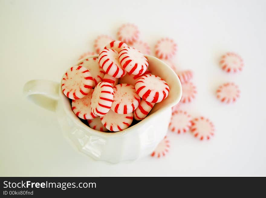 Red and white peppermint candy in  ceramic pitcher, scattered candies in background. Red and white peppermint candy in  ceramic pitcher, scattered candies in background