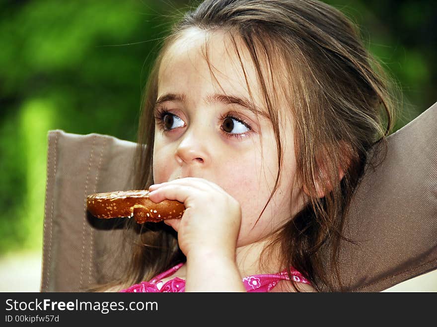 Cute little girl eating a big pretzel in an outdoor setting. Cute little girl eating a big pretzel in an outdoor setting.