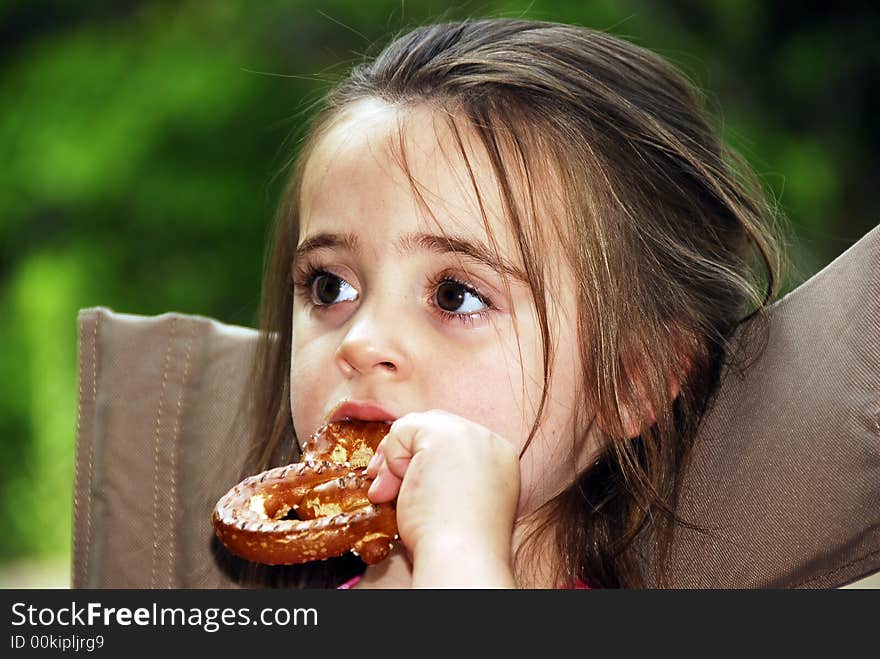 Cute little girl eating a big pretzel in an outdoor setting. Cute little girl eating a big pretzel in an outdoor setting.