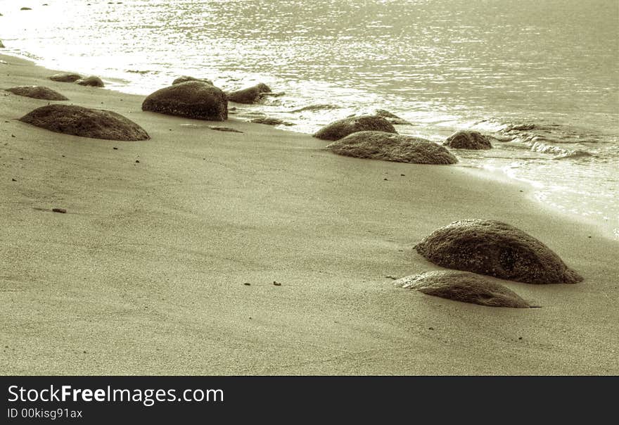 Clean rocky beach, with the sea gently breaking, at sunset. Sepia toned. Clean rocky beach, with the sea gently breaking, at sunset. Sepia toned.