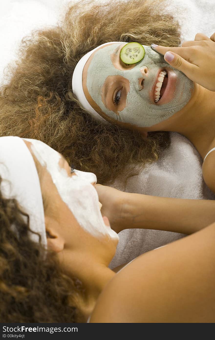 Young happy women with puryfing mask. Ther're lying on towels. Young happy women with puryfing mask. Ther're lying on towels.