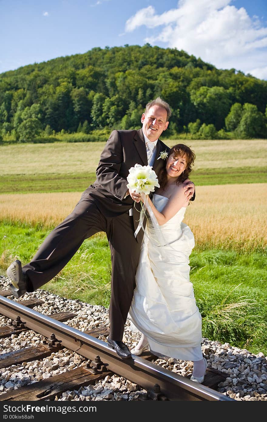 Bridal couple on rails, being in the nature. Great azure sky. Great summer! He balances on one foot on the rail. Bridal couple on rails, being in the nature. Great azure sky. Great summer! He balances on one foot on the rail.