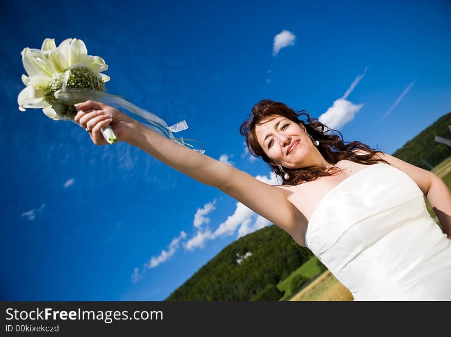 Fancy Perspective. Bride holds her bridal bouquet on outstretched arm. Deepblue sky as background. Sunny weather. Adult bride. Fancy Perspective. Bride holds her bridal bouquet on outstretched arm. Deepblue sky as background. Sunny weather. Adult bride.