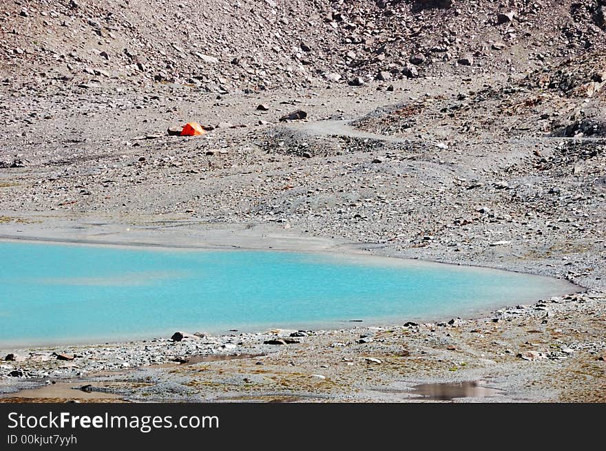 Orange tent next a blue mountain lake, Italy