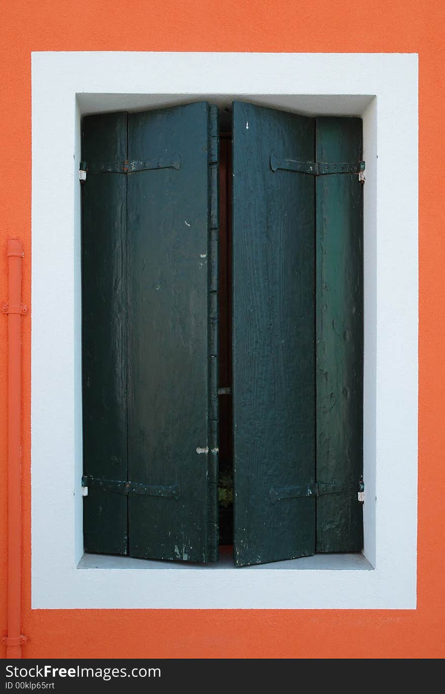 Closed window on a bright orange wall of a house on the island of Burano, outside of Venice Italy. Closed window on a bright orange wall of a house on the island of Burano, outside of Venice Italy.