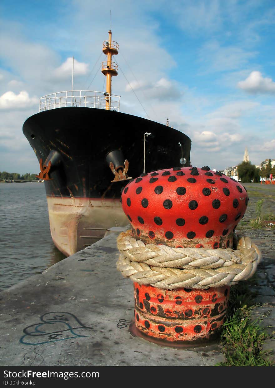 A commercial boat moored in a harbor to a red quayside bollard under a blue sky. . A commercial boat moored in a harbor to a red quayside bollard under a blue sky.