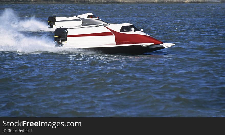 Two white formula one outboards side by side at full speed in competition on blue water of a river.