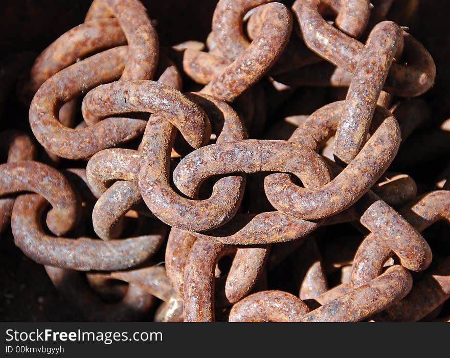 A close-up rusty chain left heaped in a pile in the sun.