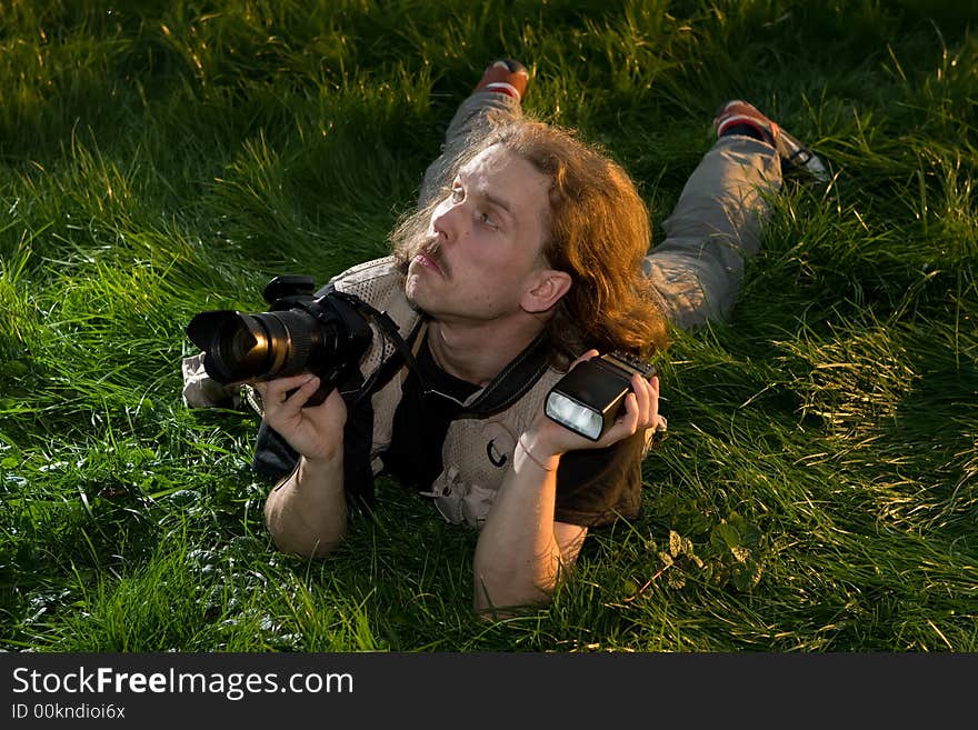 The photographer with the camera lays on a green grass. The photographer with the camera lays on a green grass