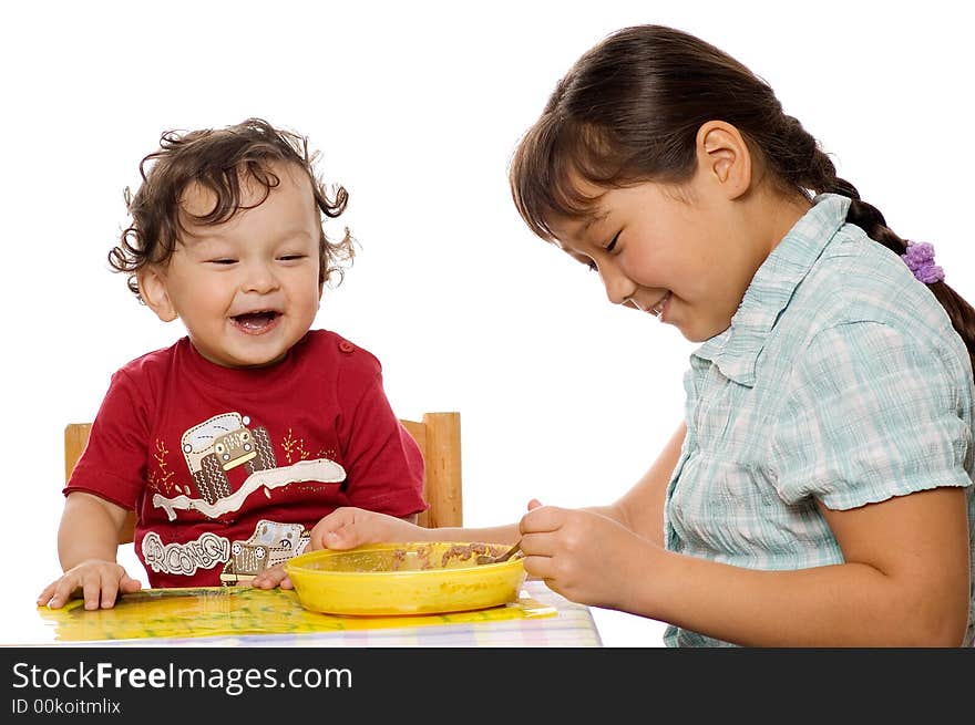 The big sister feeds the younger brother with a porridge. The big sister feeds the younger brother with a porridge.