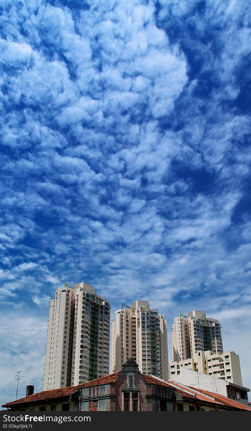 Juxtaposition of a low sprawling shop house built during colonial days in Singapore against modern towering condominium apartment blocks in the background, in a cloudy sky. Juxtaposition of a low sprawling shop house built during colonial days in Singapore against modern towering condominium apartment blocks in the background, in a cloudy sky.