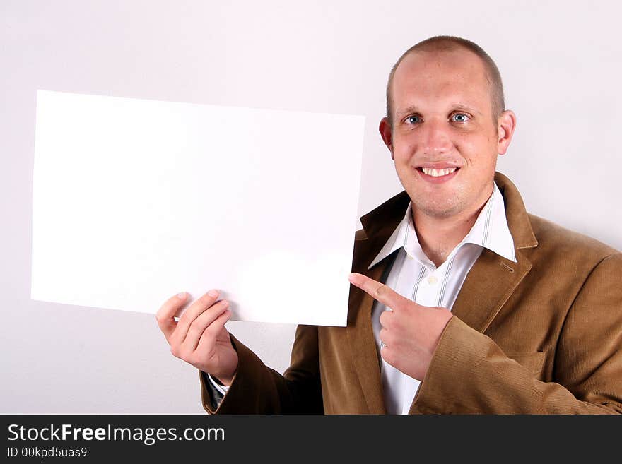 A young businessman is amiling and holds a sign and points at it! White sign to write on!. A young businessman is amiling and holds a sign and points at it! White sign to write on!