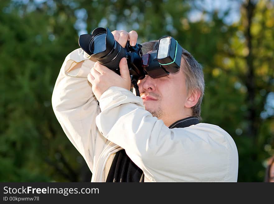 The man the photographer looks in the view-finder of the camera on a background of trees. The man the photographer looks in the view-finder of the camera on a background of trees