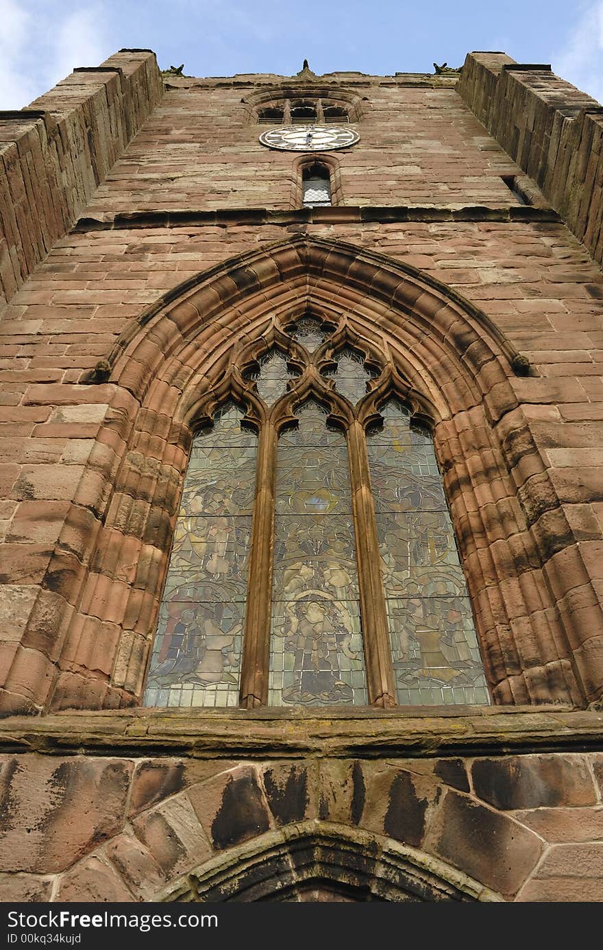 Medieval village church made from sandstone with stained glass windows and a clockface.