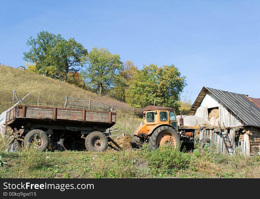 Rural landscape. An old tractor with the trailer about a shabby shed with hay. The photo is filled by mood of a rural life.