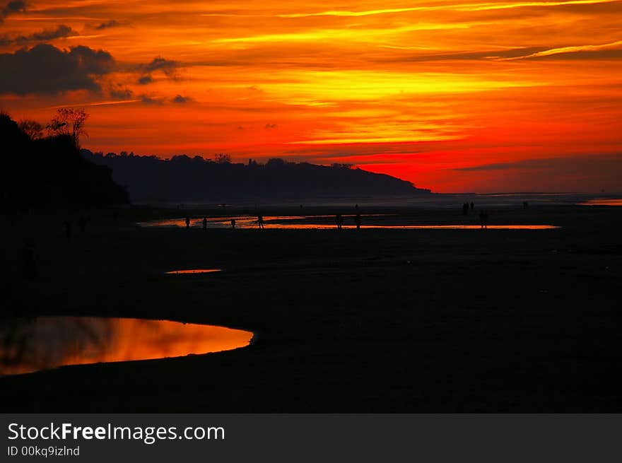 A colourful dusk on a large beach where people, couples are walking quietly. A colourful dusk on a large beach where people, couples are walking quietly.