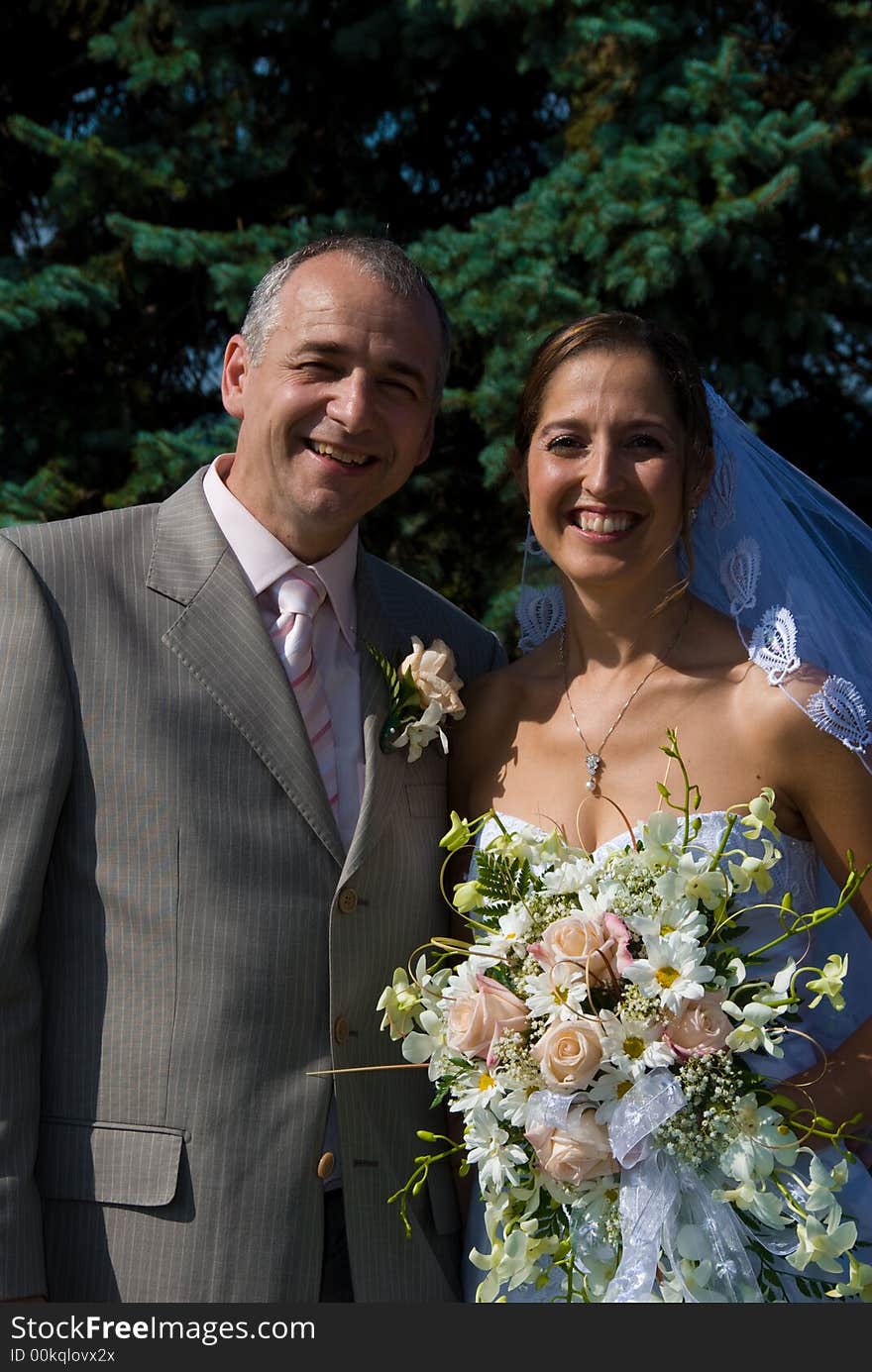 A bride and a groom posing behind some trees. A bride and a groom posing behind some trees