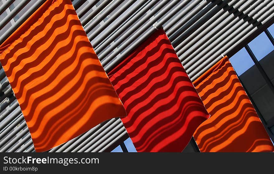 Ceiling's cross beams' shadows falling on bright red and orange flags creating a changing moving pattern on these flags