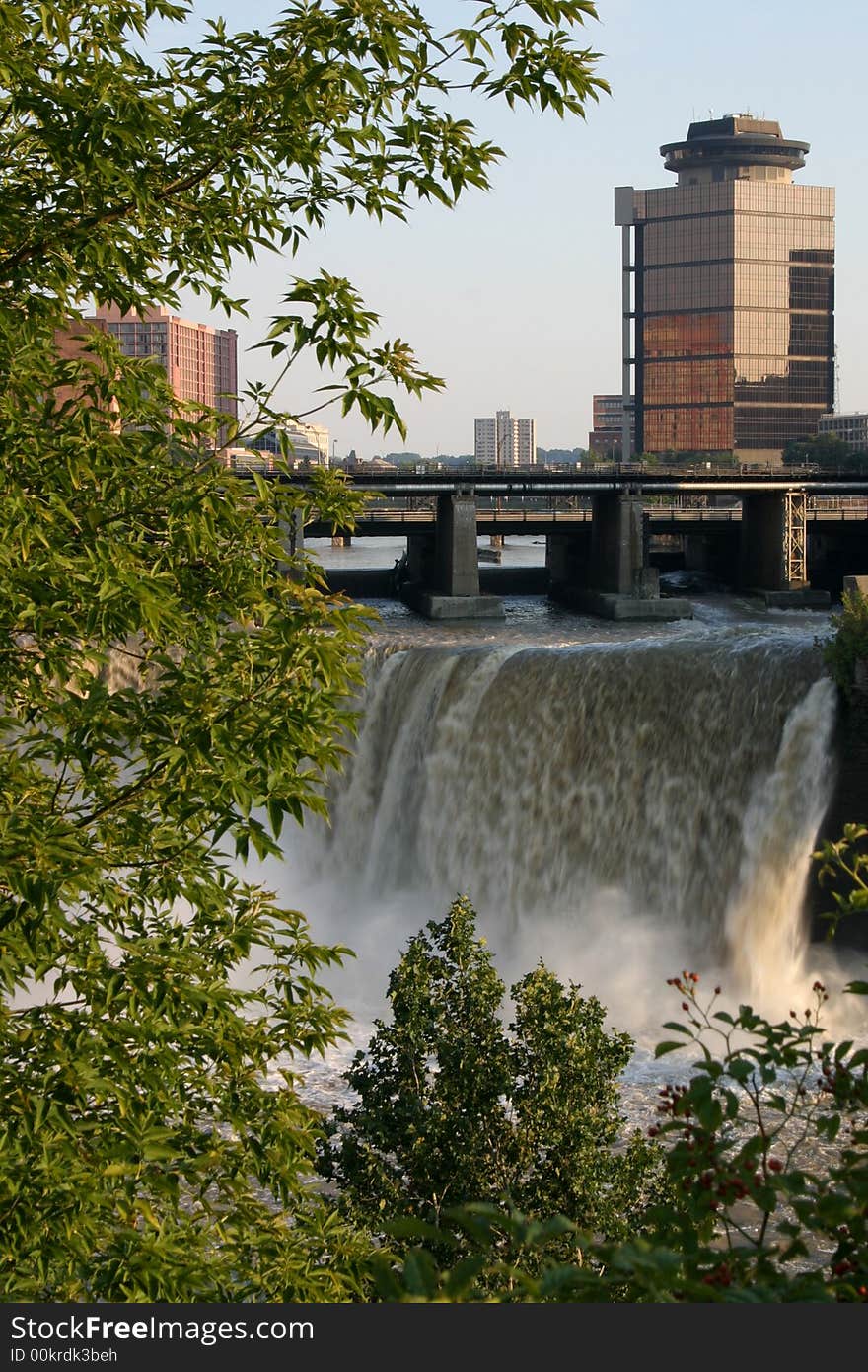 City skyling above Waterfalls.  Leafy green branches in the foreground. City skyling above Waterfalls.  Leafy green branches in the foreground.