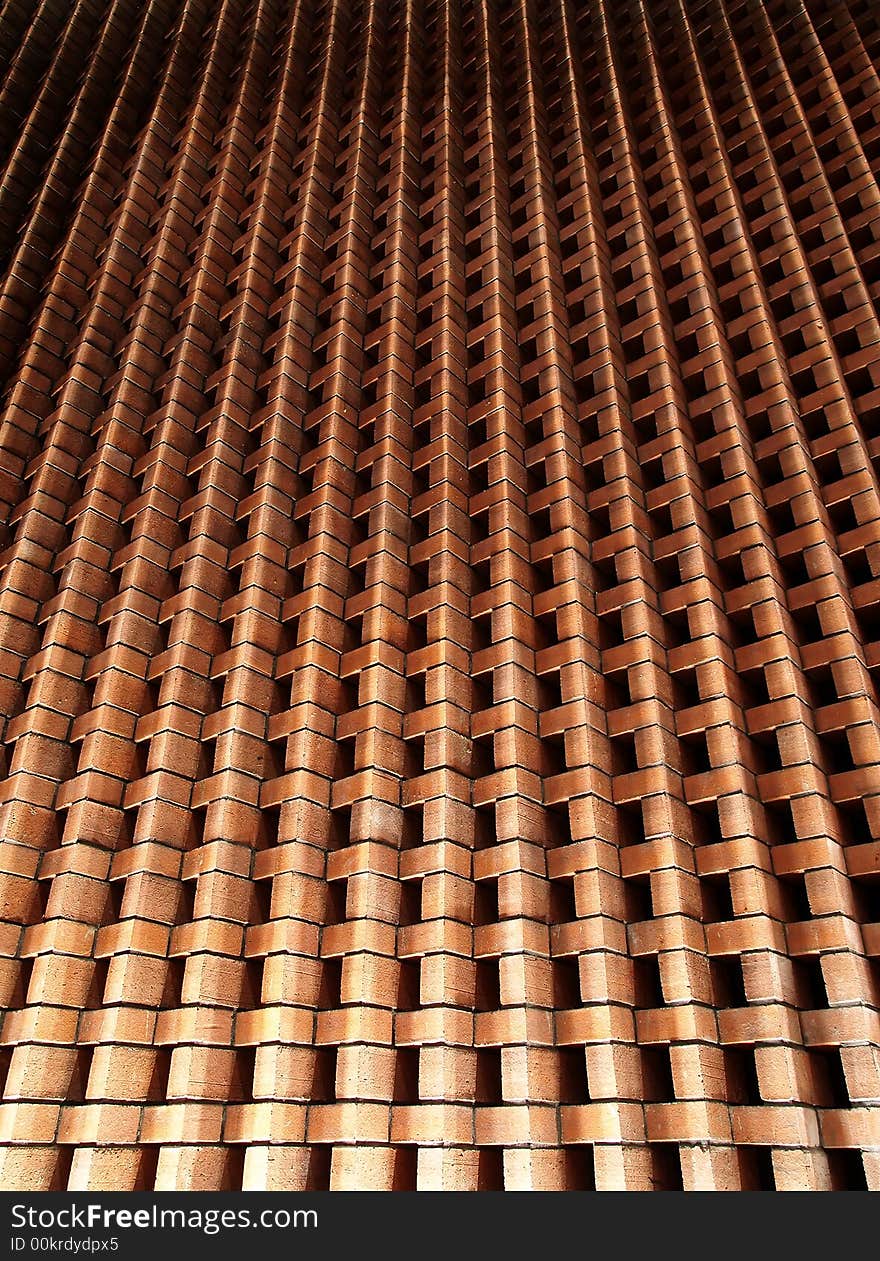 A upward converging perspective of an up-lighted brick wall created by stacking bricks in an alternating angular arrangement.