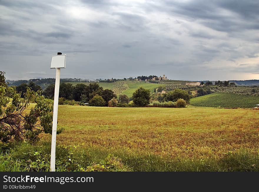 Pole with blank sign overlooking Tuscan hills with dramatic sky