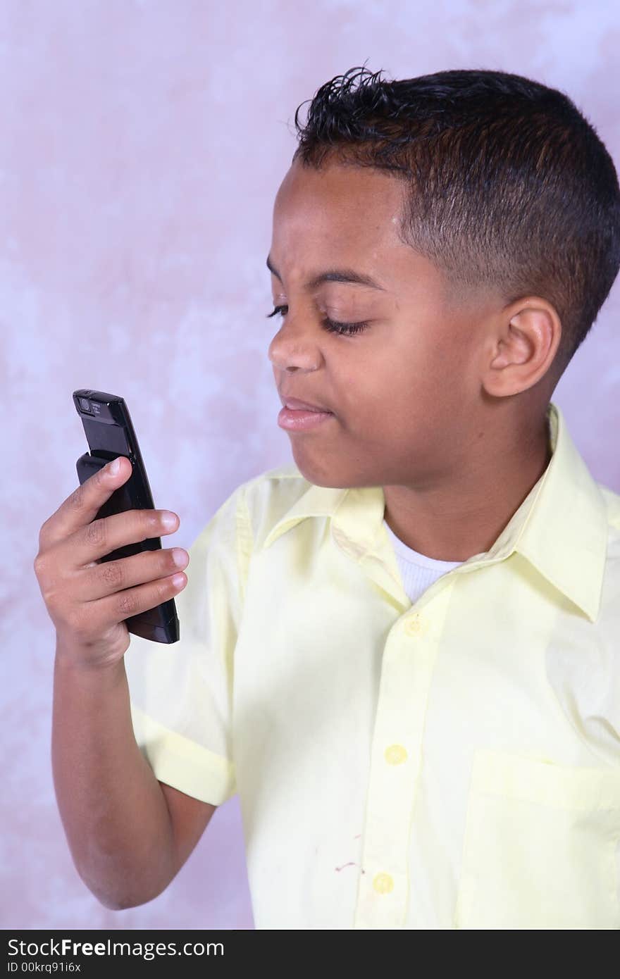 A young boy holding a cell phone looking at it in discust. A young boy holding a cell phone looking at it in discust