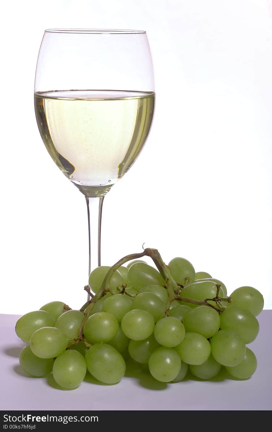 A glass of white wine and grapes, on white. A glass of white wine and grapes, on white