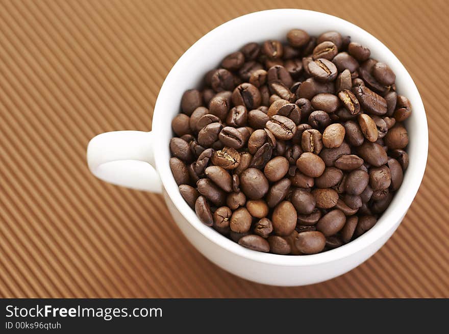 Coffee cup filled with coffee beans over a brown background